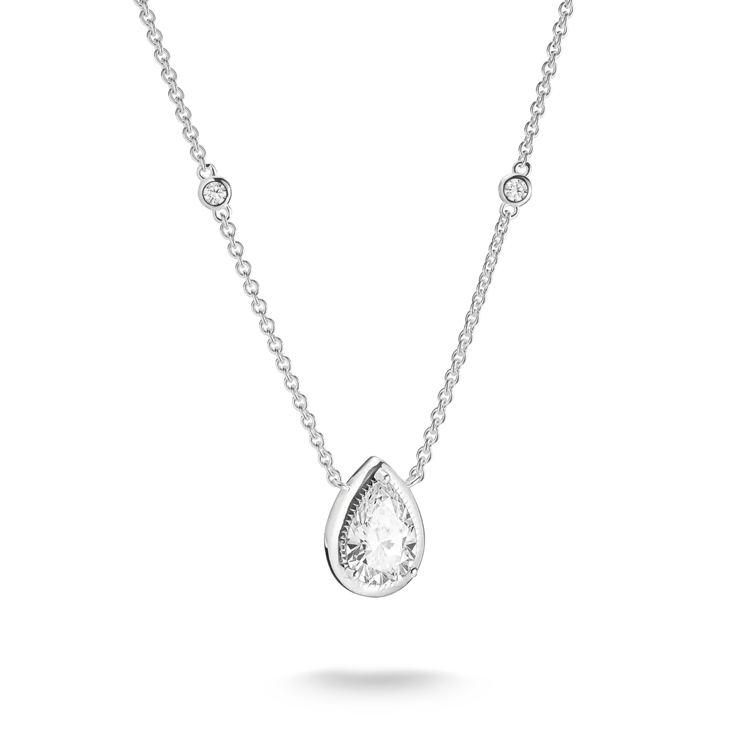 A silver-toned necklace featuring a pear-cut clear gemstone pendant in a prong setting, with a delicate chain accented by two small round bezel-set stones, shown on a white background with a soft shadow.