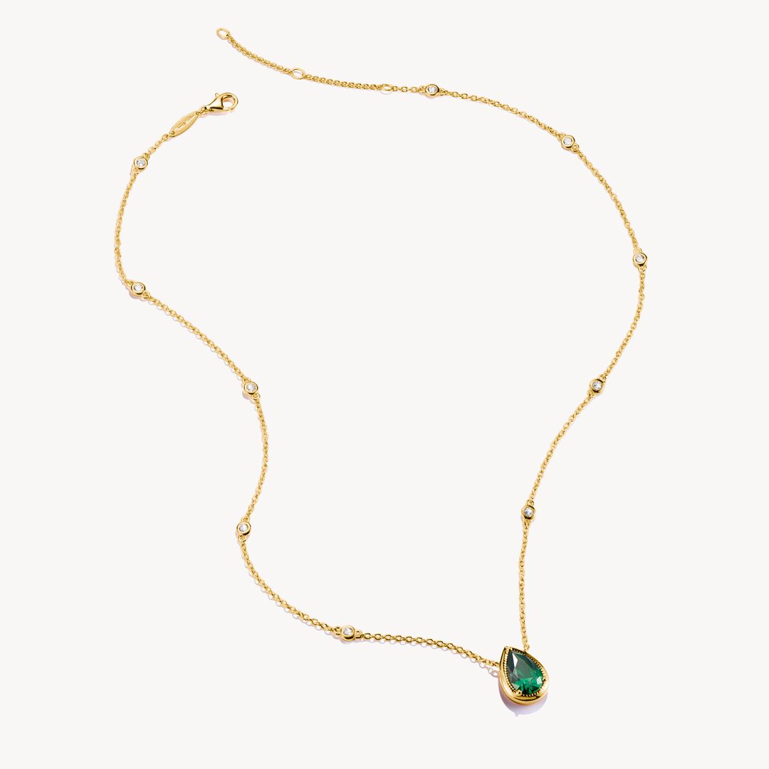 Gold necklace with a green teardrop pendant on a white background