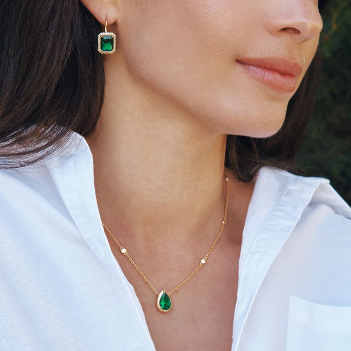 Close-up of a woman wearing gold earrings and necklace with green gemstones.