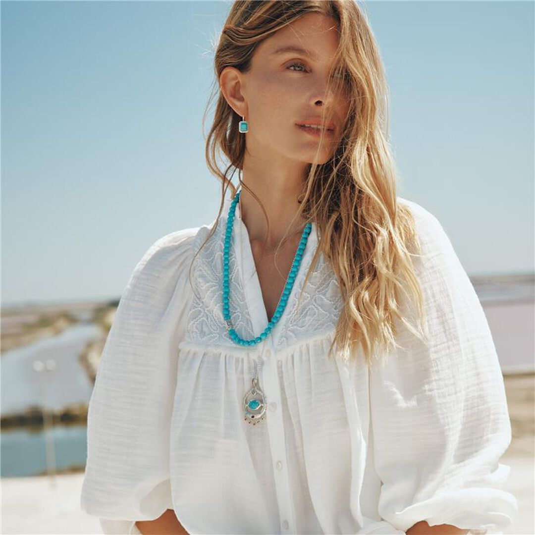Woman wearing a white blouse and turquoise jewelry with a blurred coastal background