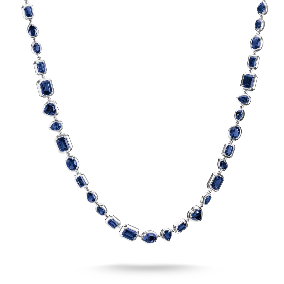 A silver-toned necklace featuring multiple strands of deep blue gemstones in varied shapes, including emerald, round, and marquise cuts, displayed against a clean white background.