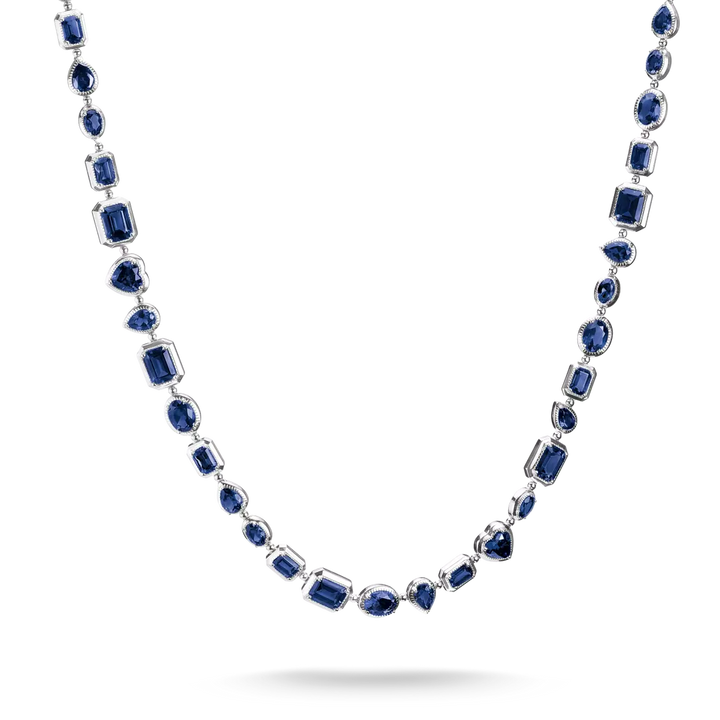 A silver-toned necklace featuring multiple strands of deep blue gemstones in varied shapes, including emerald, round, and marquise cuts, displayed against a clean white background.