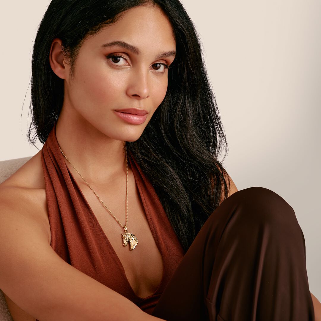 Woman wearing a rust-colored top and brown pants with a neutral background