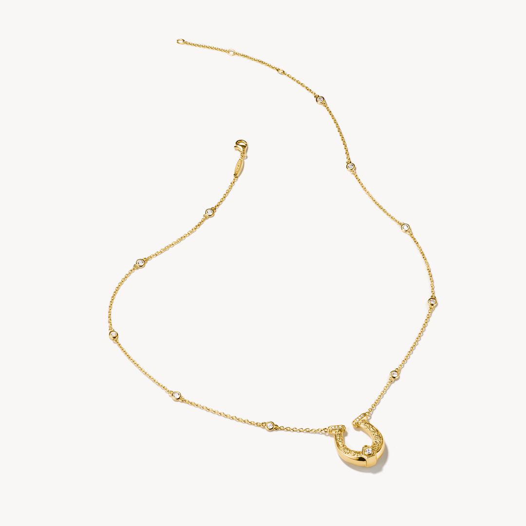 Gold horseshoe necklace with small diamonds on a white background