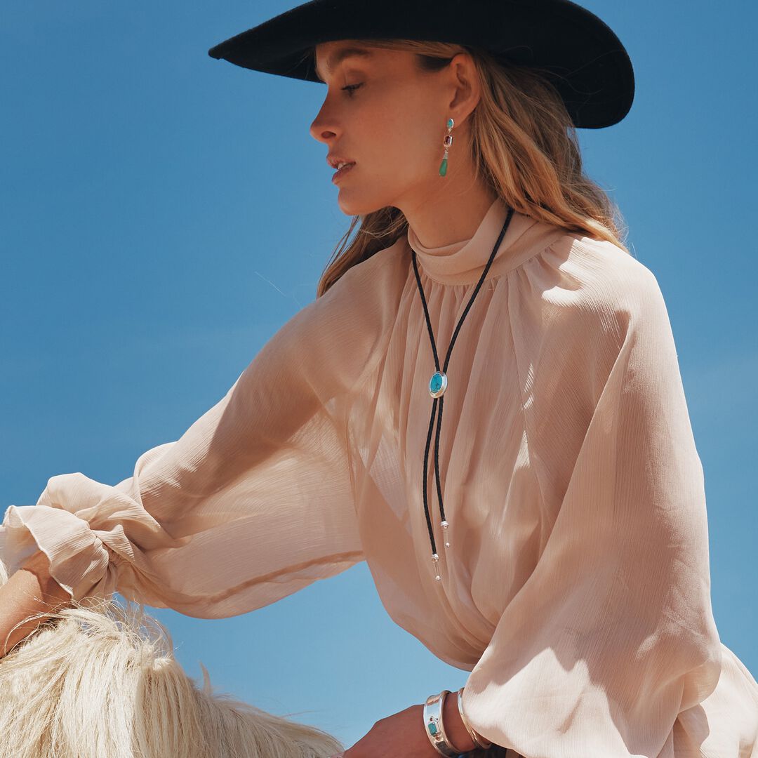 Woman wearing a beige blouse and black hat against a clear blue sky