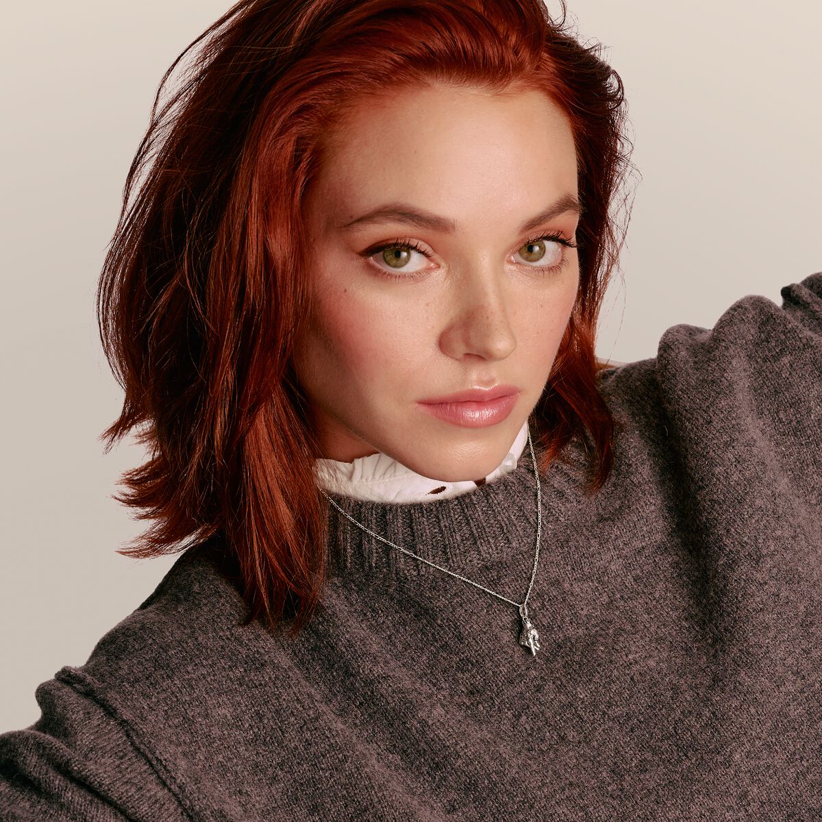Woman with red hair wearing a gray sweater against a beige background