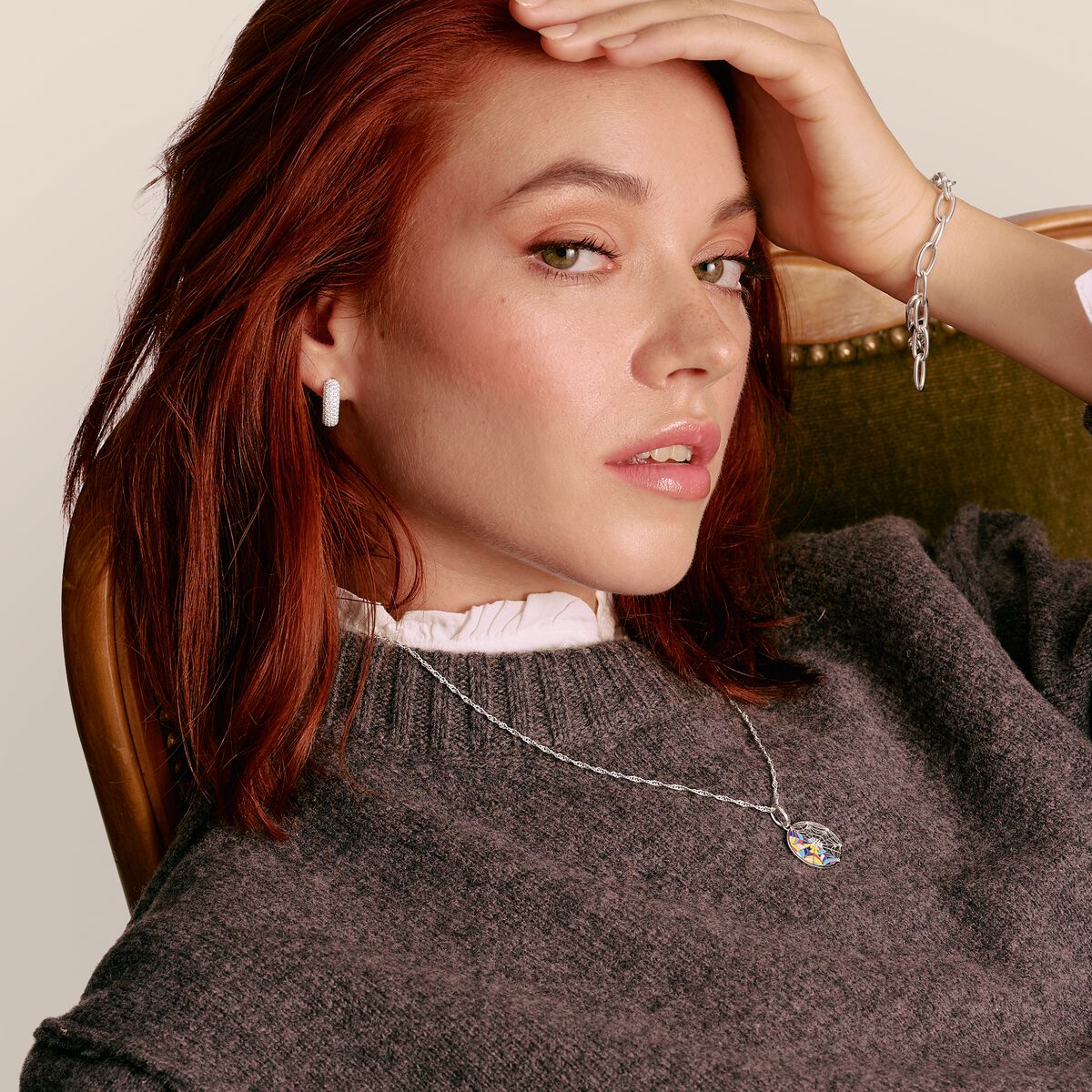 Woman wearing a necklace with a pendant, sitting in a chair.