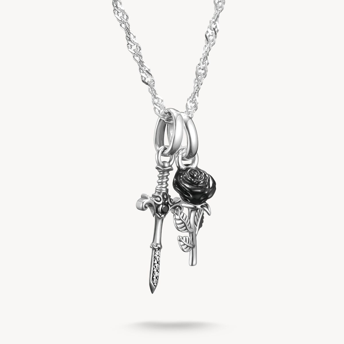 Silver necklace with a black rose and skeleton hand pendant on a white background