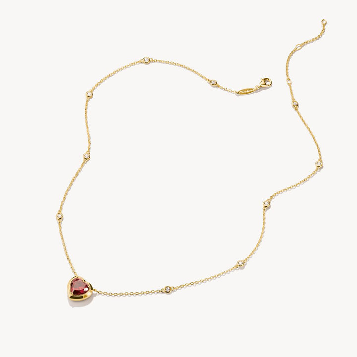 Gold necklace with a heart-shaped red gemstone on a white background