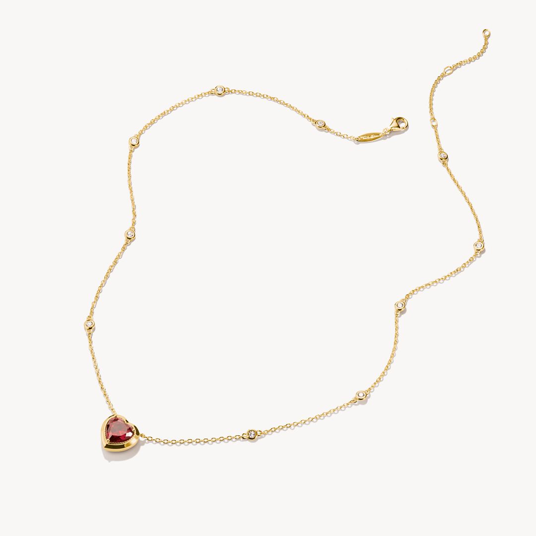 Gold necklace with a heart-shaped red gemstone pendant on a white background