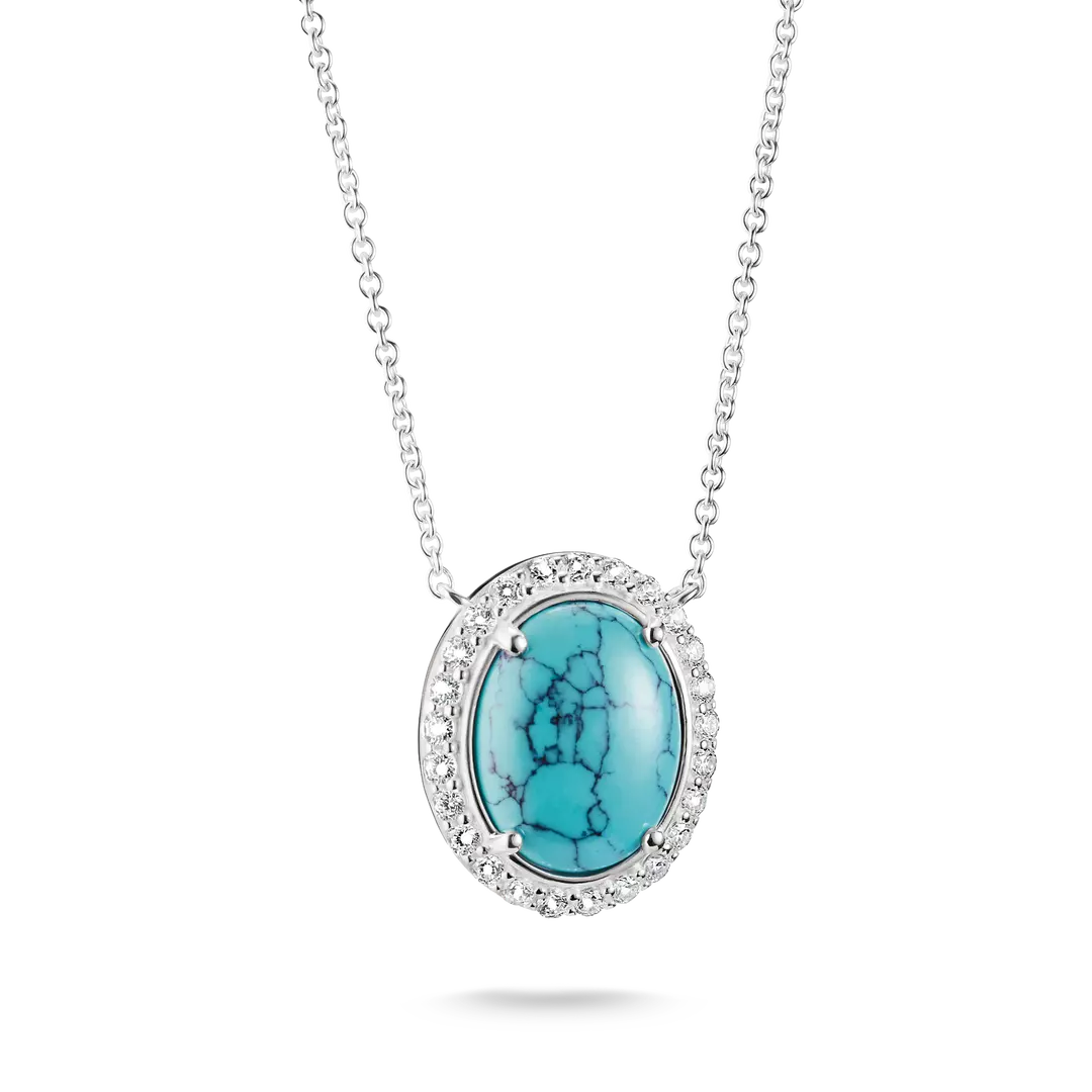 An oval pendant necklace featuring a vibrant turquoise stone with black matrix veining, surrounded by a halo of small clear stones and set in silver-toned metal, suspended from a delicate silver chain against a white background.