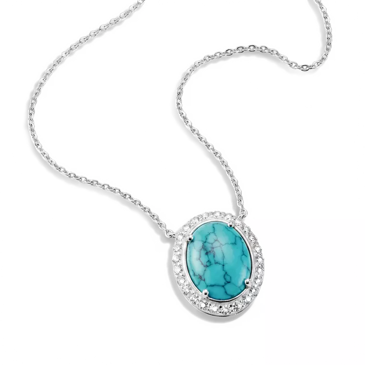 Silver oval pendant necklace featuring a turquoise-colored stone with black matrix veining, surrounded by a halo of small clear stones on a white background.