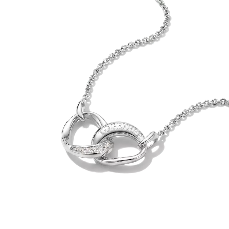 A silver interlocking heart pendant necklace on a delicate silver chain, featuring a small row of clear stones on one heart and the word 'TOGETHER' engraved on the other, set against a clean white background.