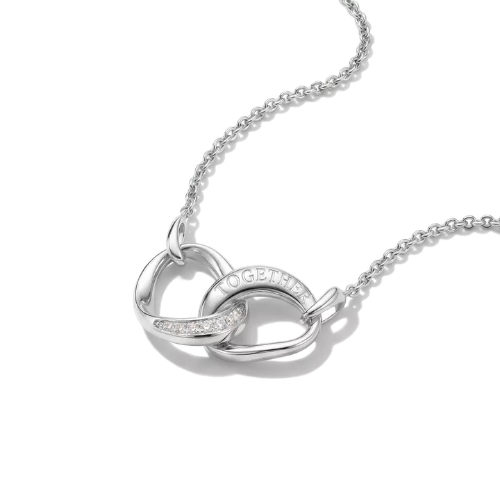 A silver interlocking heart pendant necklace on a delicate silver chain, featuring a small row of clear stones on one heart and the word 'TOGETHER' engraved on the other, set against a clean white background.