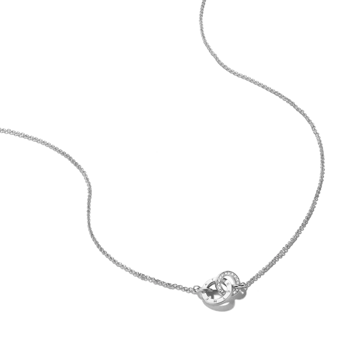 A delicate silver chain necklace featuring a small heart-shaped pendant with a clear central gemstone and a tiny round accent stone, shown on a plain white background.