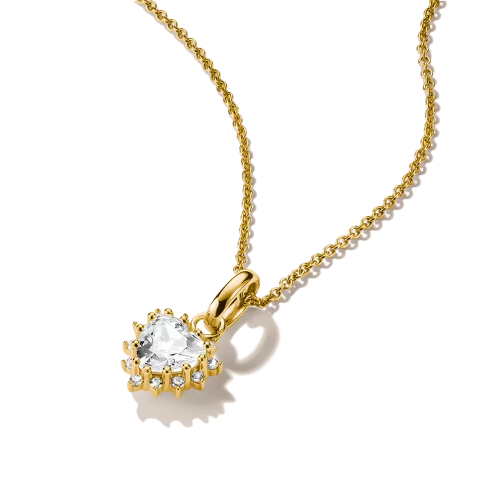 A gold pendant necklace featuring a heart-shaped clear gemstone surrounded by small sparkling accents, suspended from a delicate gold chain on a white background.