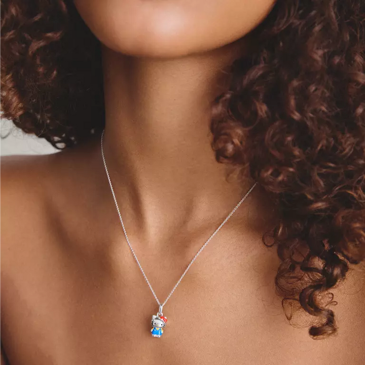 A close-up of a model wearing a delicate silver chain necklace with a small, colorful pendant featuring a cartoon character in red, white, and blue.