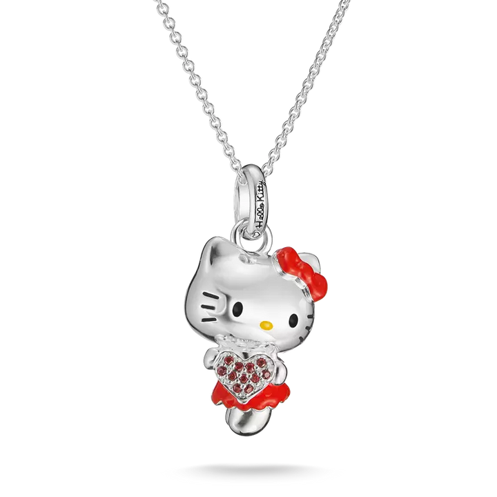 A silver Hello Kitty pendant necklace featuring a silver Hello Kitty figure with a red bow, red dress, and a red heart-shaped crystal heart, suspended on a silver chain against a white background.