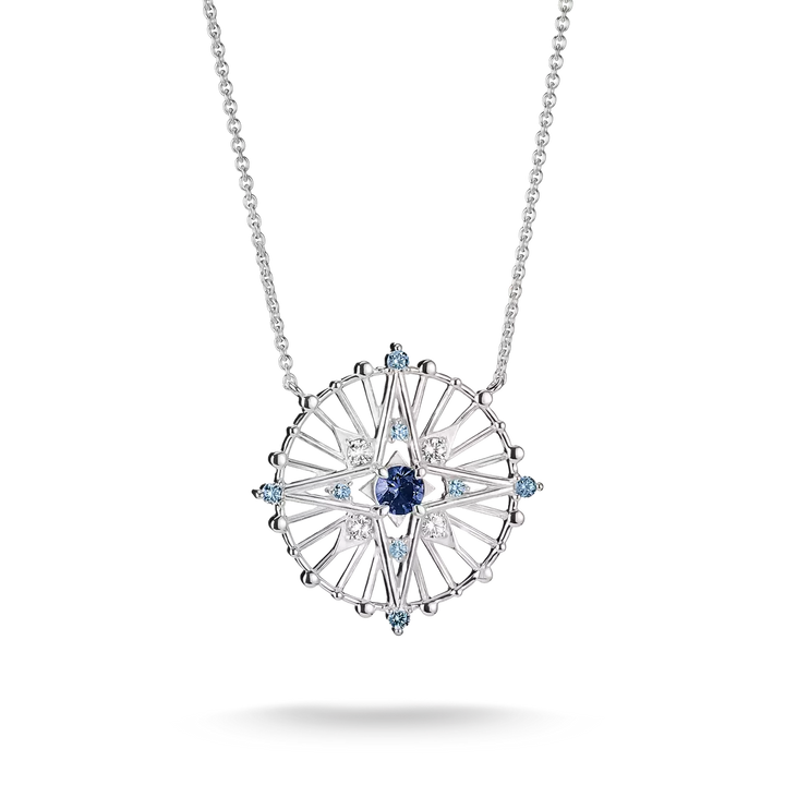 A silver-toned circular pendant necklace featuring a central deep blue sapphire surrounded by clear and light blue accent stones, suspended from a delicate silver chain on a white background.