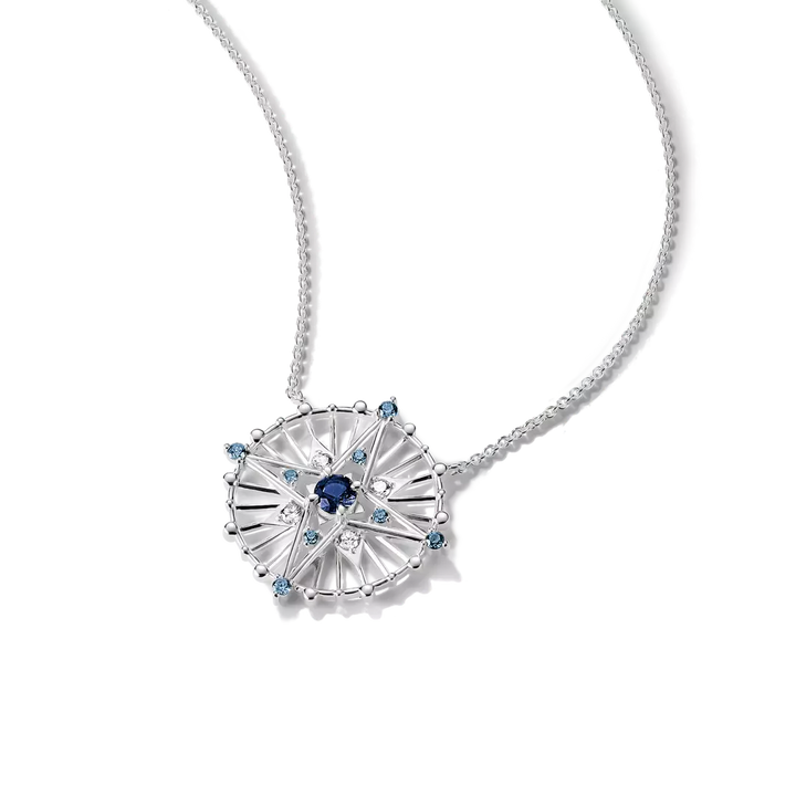 A silver-toned necklace featuring a circular sunburst pendant with a central dark blue gemstone and small light blue accent stones, shown on a clean white background.