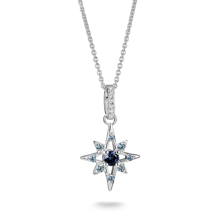 A silver-toned starburst pendant necklace featuring a central dark blue gemstone surrounded by small light blue and clear stones, suspended from a delicate silver chain on a white background.