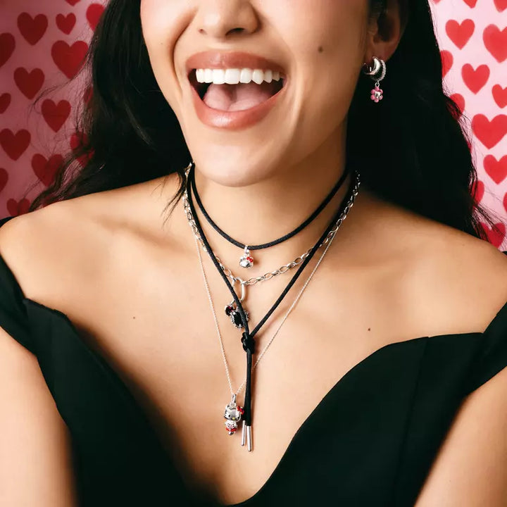 A close-up lifestyle shot of a woman wearing a layered necklace set. The necklace features black cords, silver chains, and a long pendant with a silver key and a small pink heart charm.