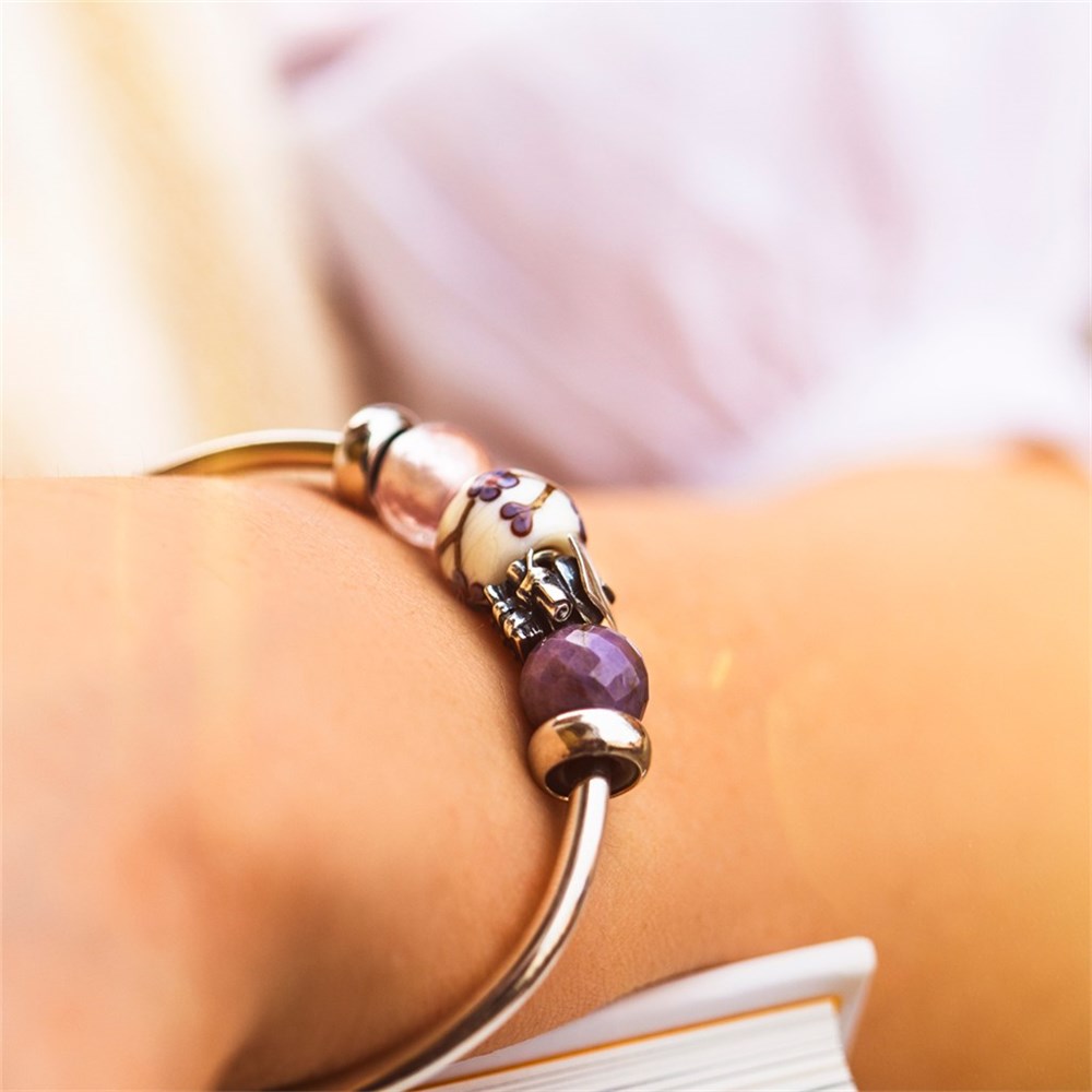 Gold bracelet with purple bead on a wrist against a blurred background