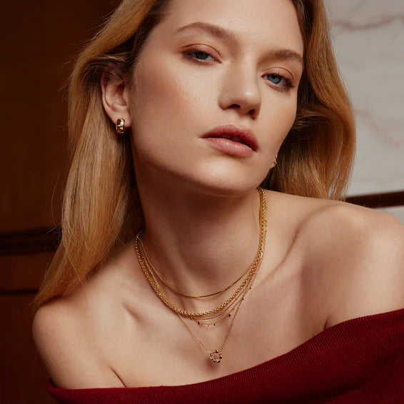 Woman wearing gold necklaces and earrings with a blurred background