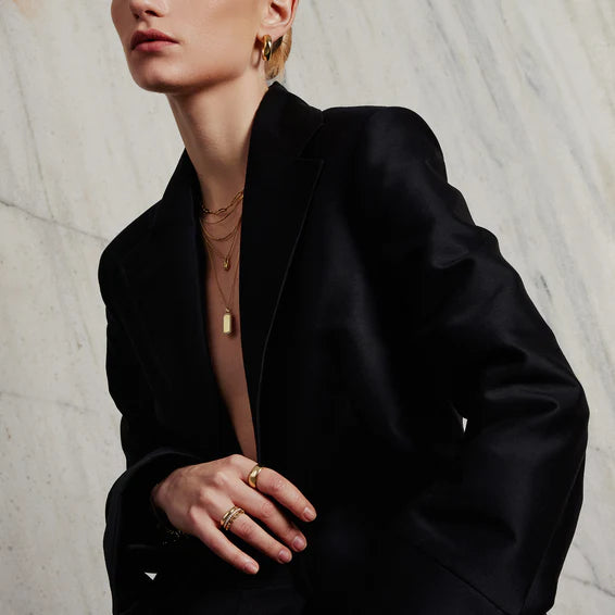 Person wearing a black blazer with gold jewelry against a textured white background