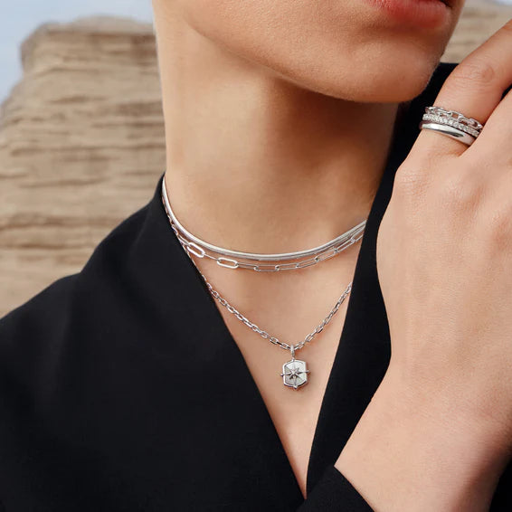 Person wearing a silver necklace and ring with a blurred natural background