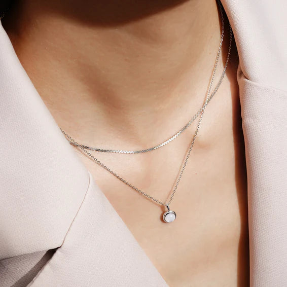 Necklace with a small round pendant worn by a person against a neutral background