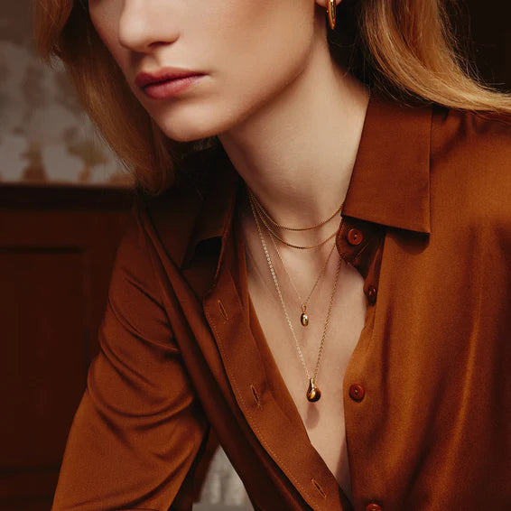 Close-up of a person wearing a brown shirt with visible jewelry.