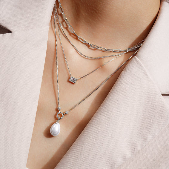 Layered silver necklaces with pendants on a person wearing a light-colored outfit.