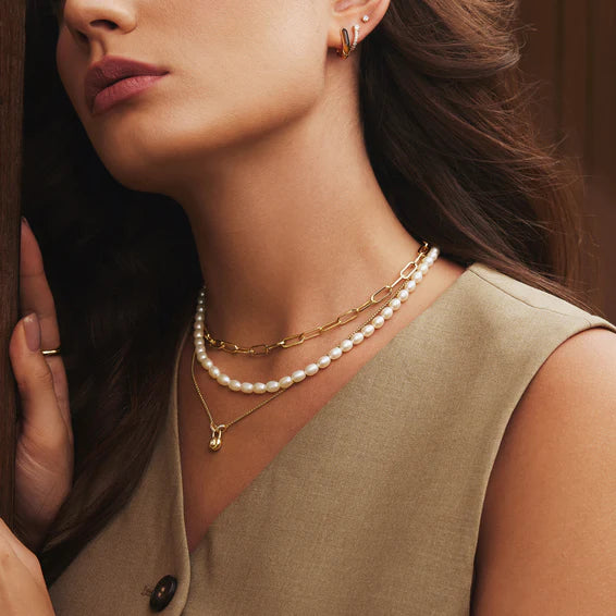 Close-up of a woman wearing gold necklaces and earrings with a neutral background