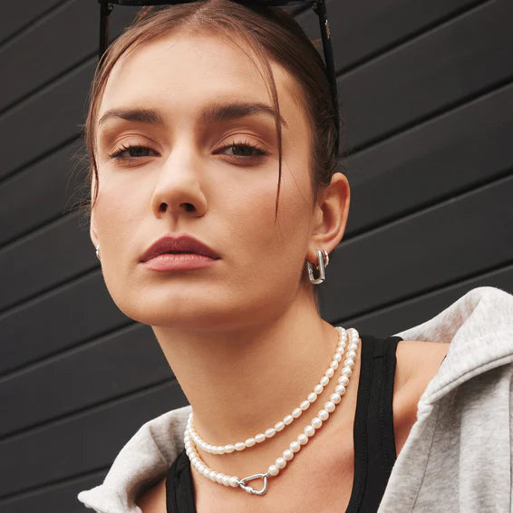 Woman wearing a pearl necklace and earrings against a black background