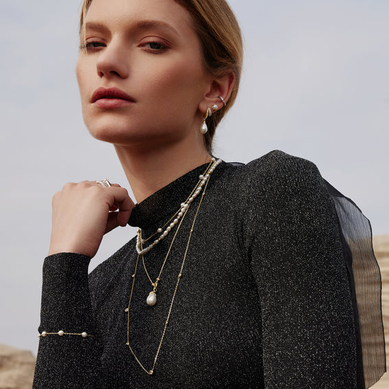 Woman wearing layered pearl necklaces and earrings against a neutral background
