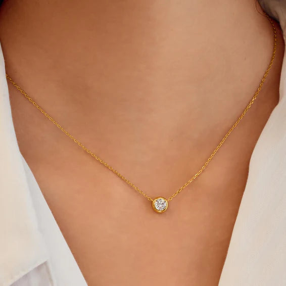 Gold necklace with a diamond pendant on a person wearing a white top.