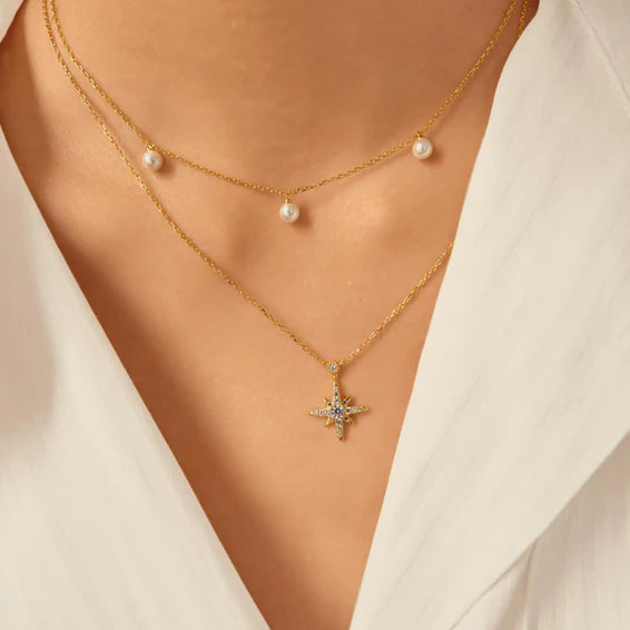 Gold necklace with star pendant worn by a person against a neutral background