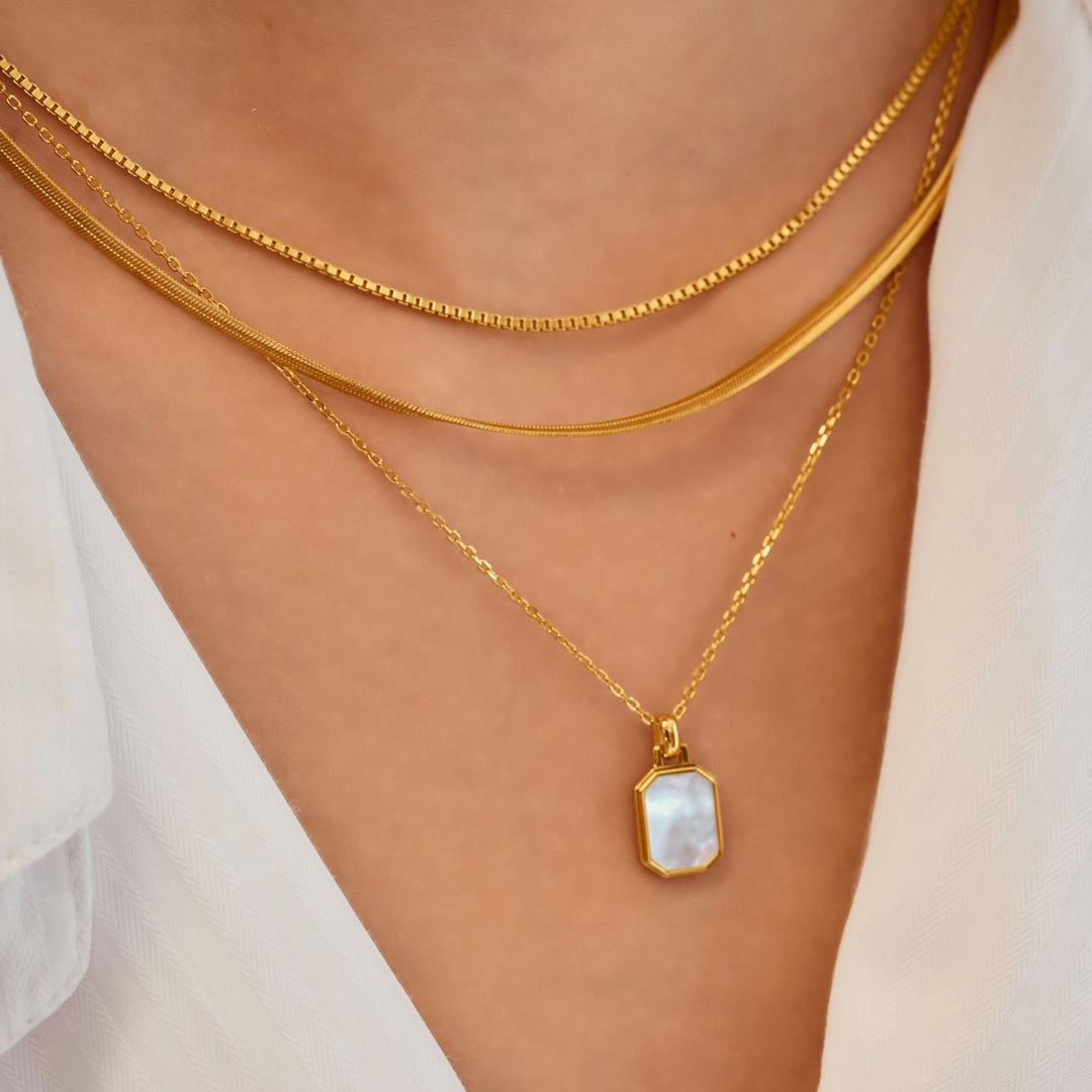 Gold necklace with a pendant on a person wearing a white top.