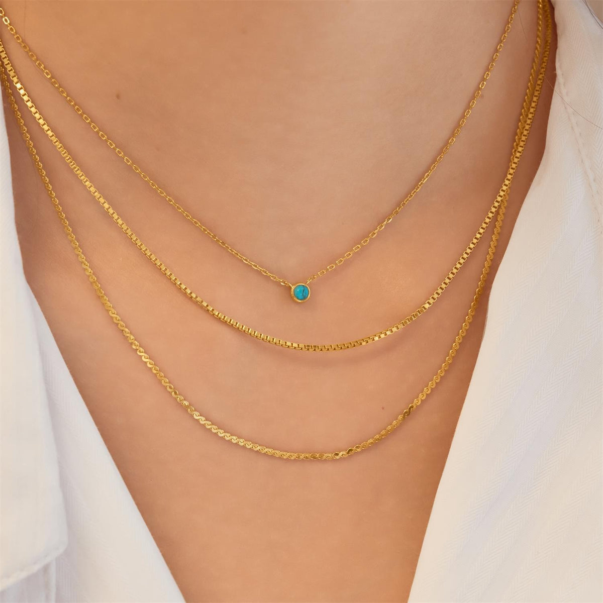 Gold chain necklace with a green gemstone on a person wearing a white top.