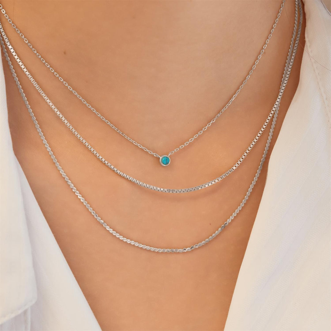 Silver chain necklace with a turquoise pendant on a person wearing a white top.