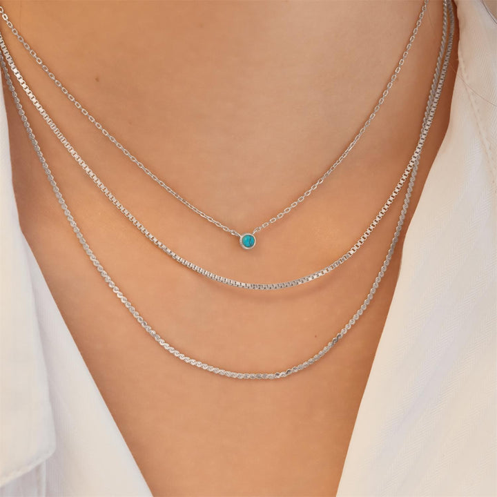 Silver chain necklace with a turquoise pendant on a person wearing a white top.