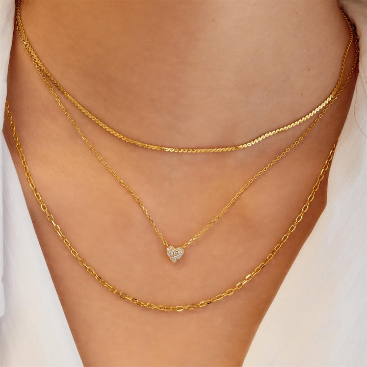 Gold chain necklace with a heart-shaped pendant on a person's neck.