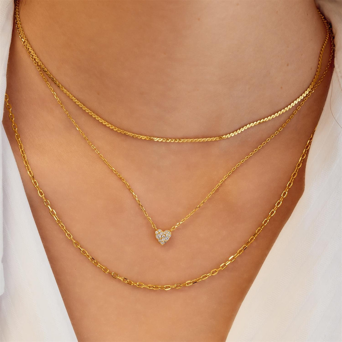 Gold chain necklace with a heart-shaped pendant on a person's neck.
