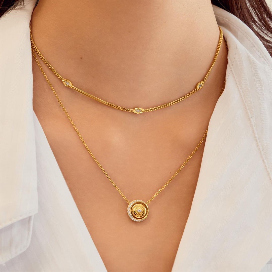Gold necklace with a circular pendant on a person wearing a white shirt.