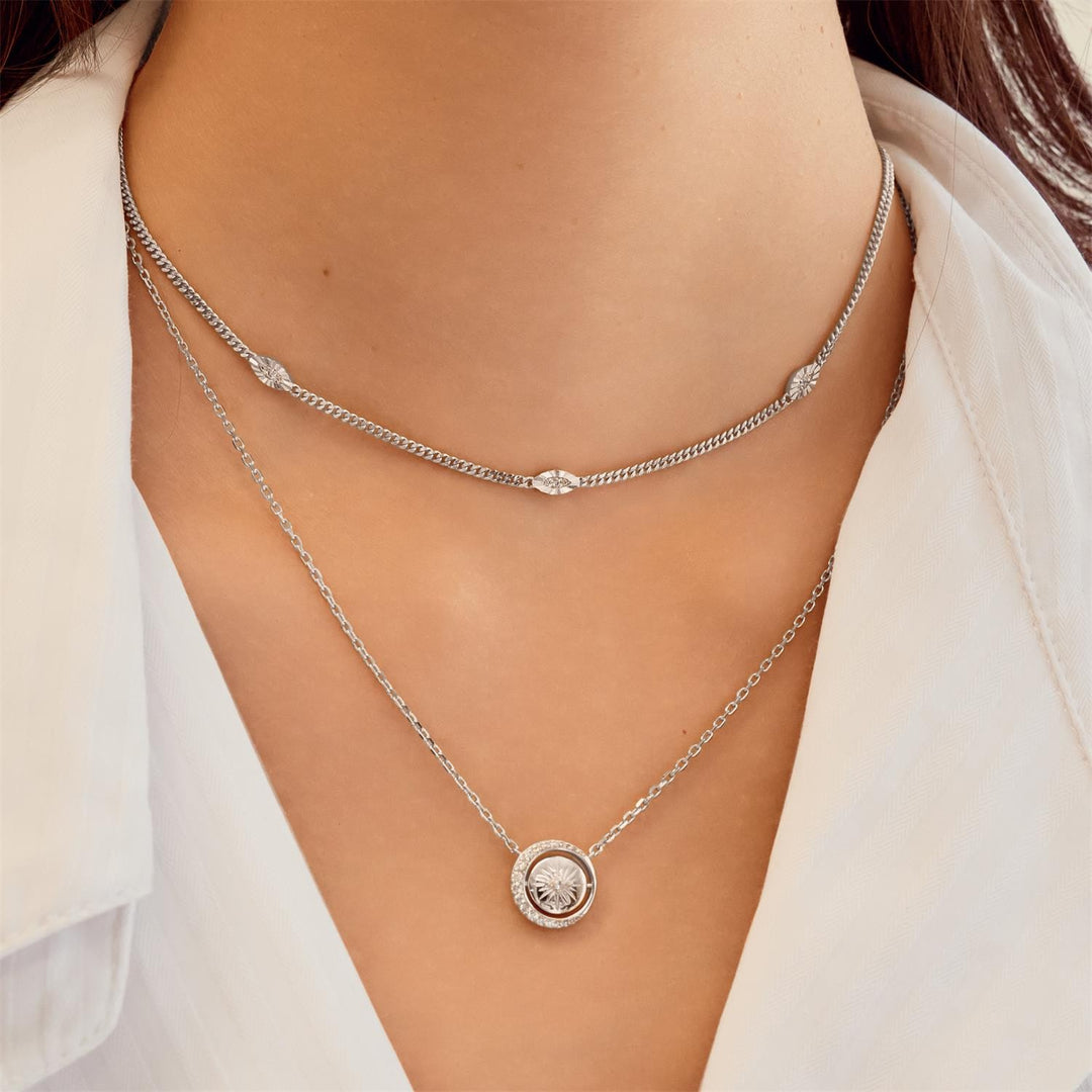 Silver necklace with a round pendant on a person wearing a white shirt.