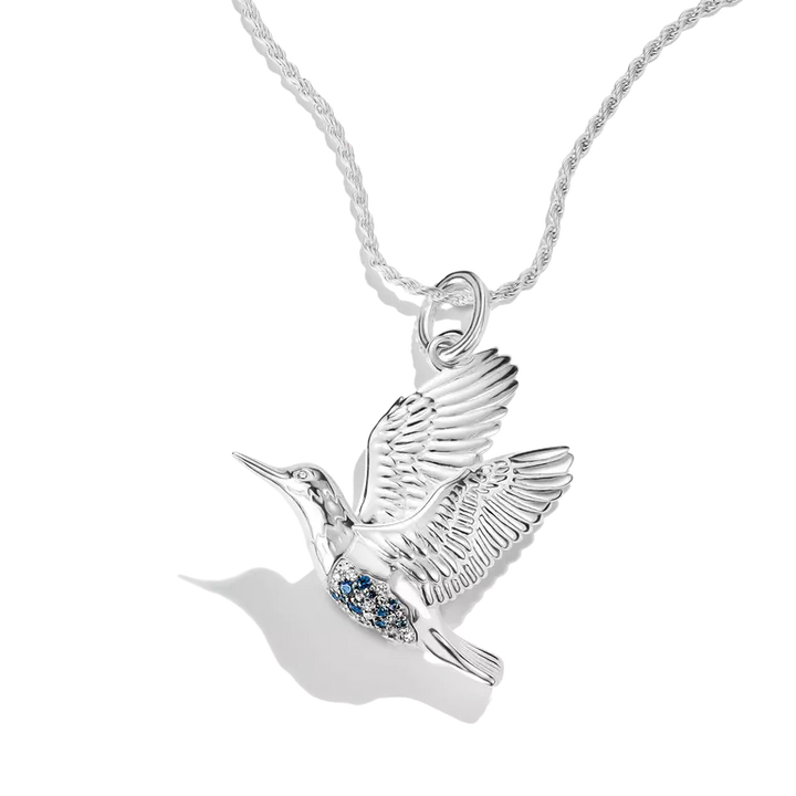 A sterling silver hummingbird pendant necklace with a small cluster of blue gemstones on its chest, suspended from a matching silver rope chain against a white background.