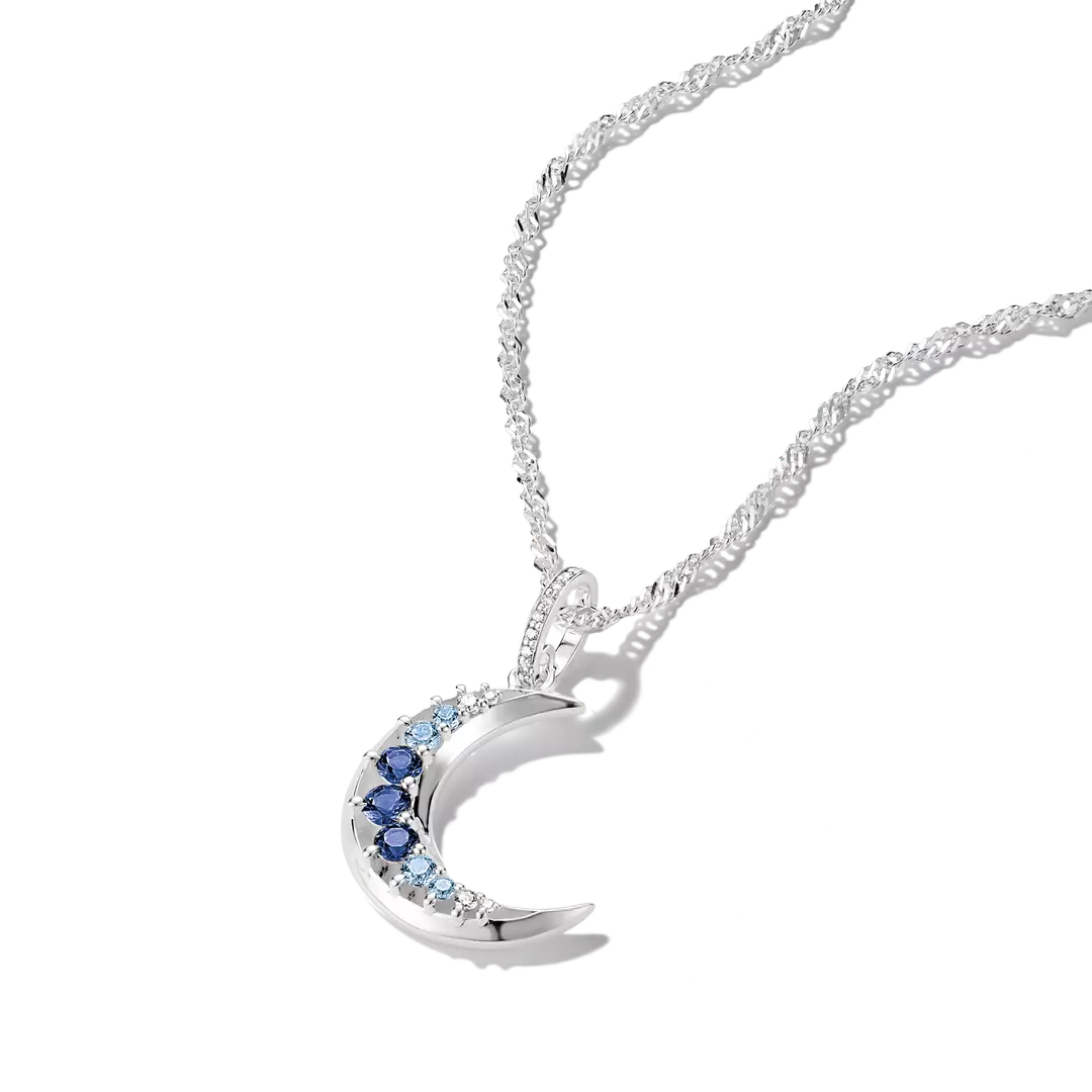 A silver crescent moon pendant necklace with a row of small light blue stones and three darker blue stones, shown on a white background.