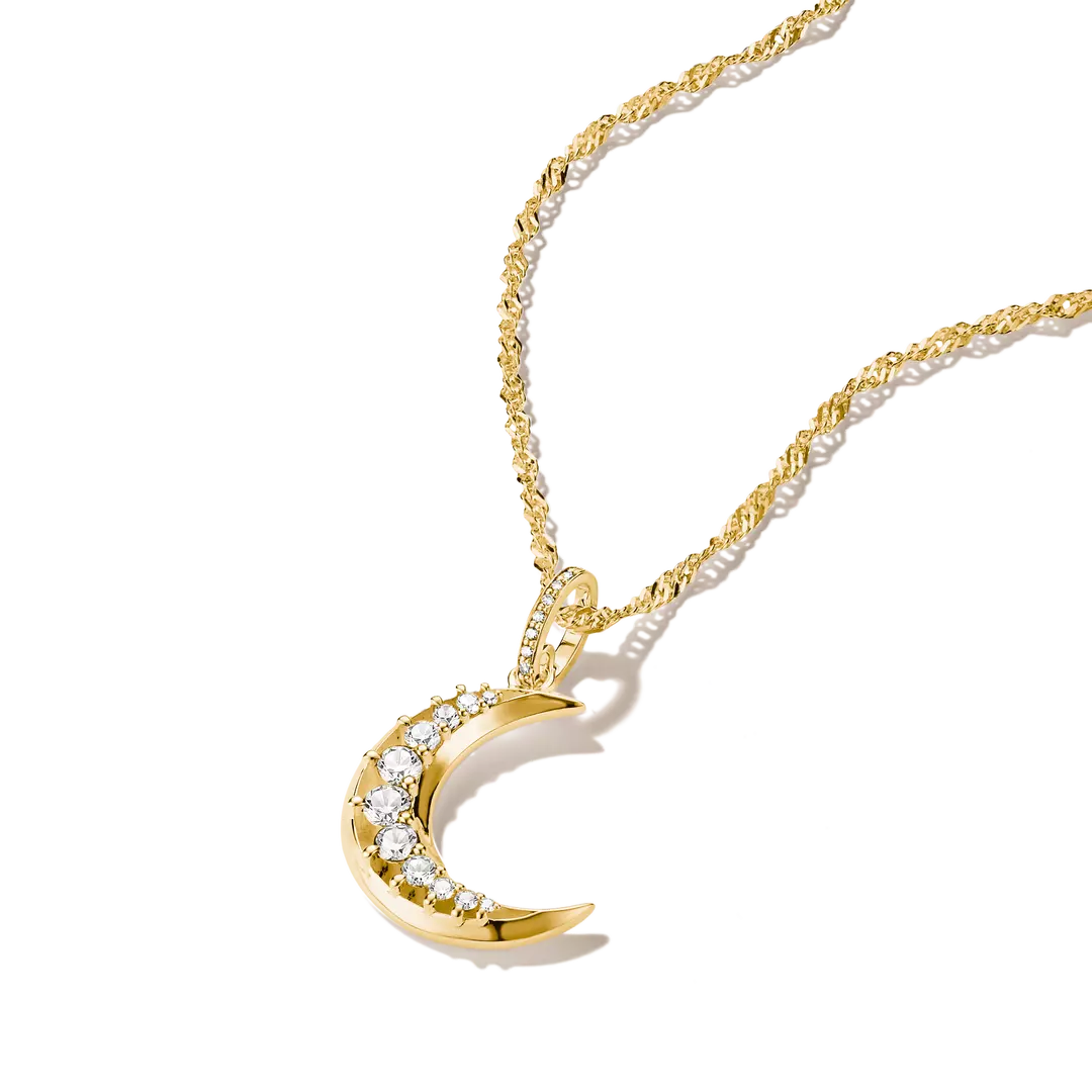 A gold crescent moon pendant necklace adorned with clear crystals, shown on a clean white background with a soft shadow.