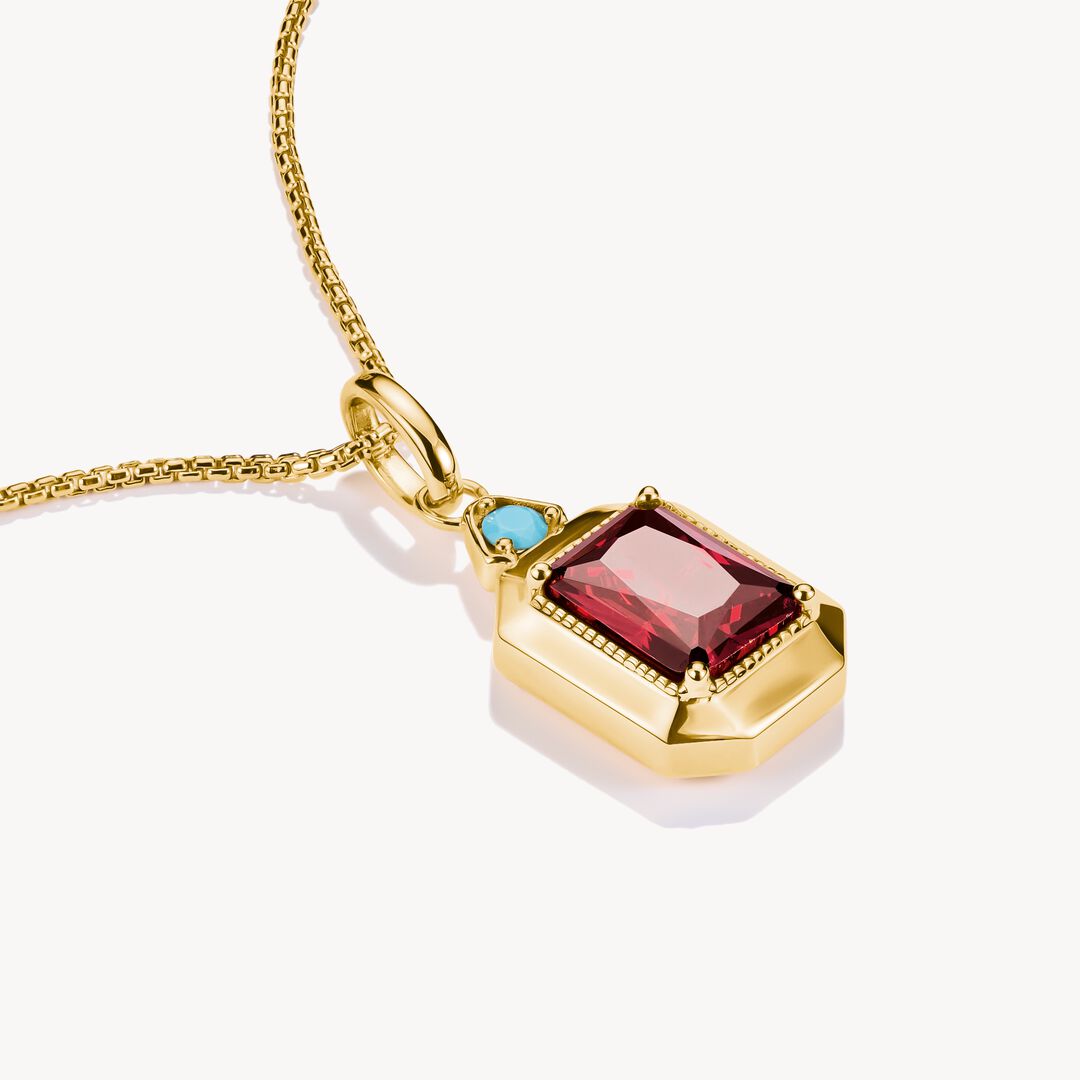 Gold necklace with a pendant featuring red and blue gemstones on a white background